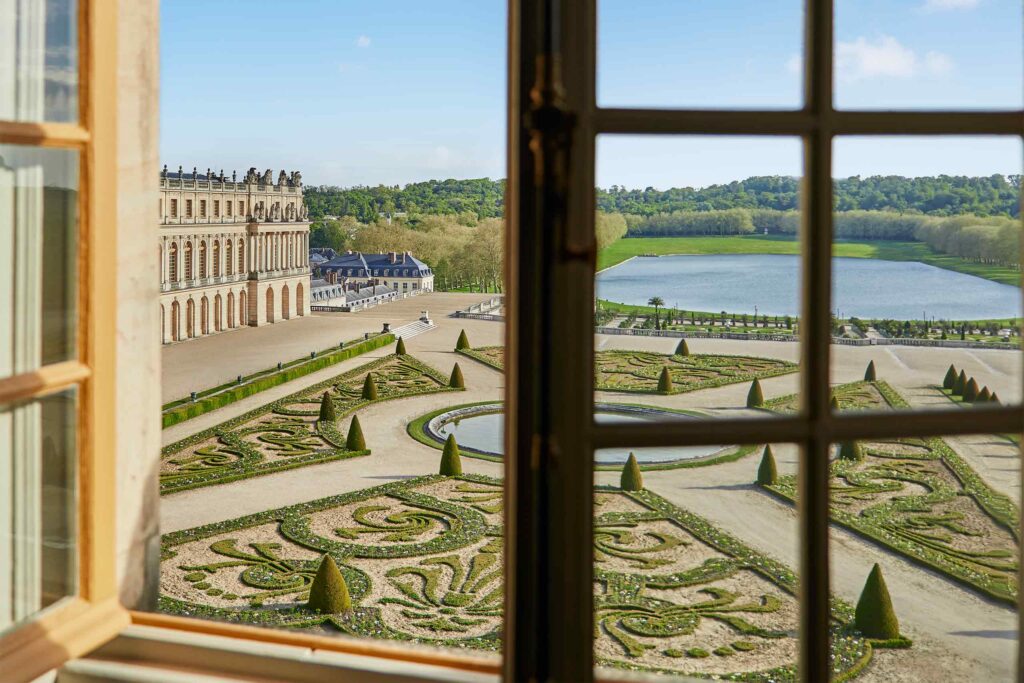 Views from a window at Airelles Château de Versailles reveal manicured gardens.