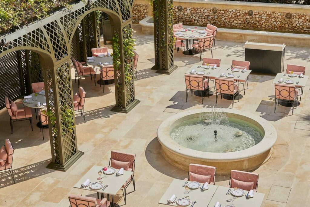 Overhead view of a terrace at Airelles Château de Versailles with pink garden chairs and a fountain.