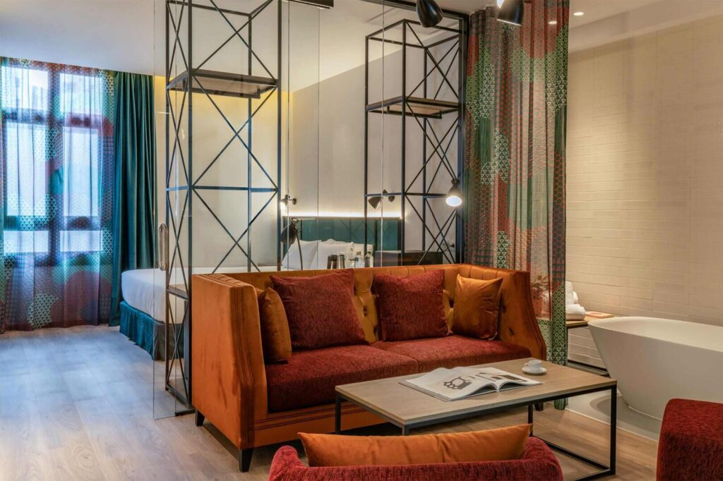 A suit at Axel Bilbao with an orange sofa in front of a table. Metal shelves stand behind it. 