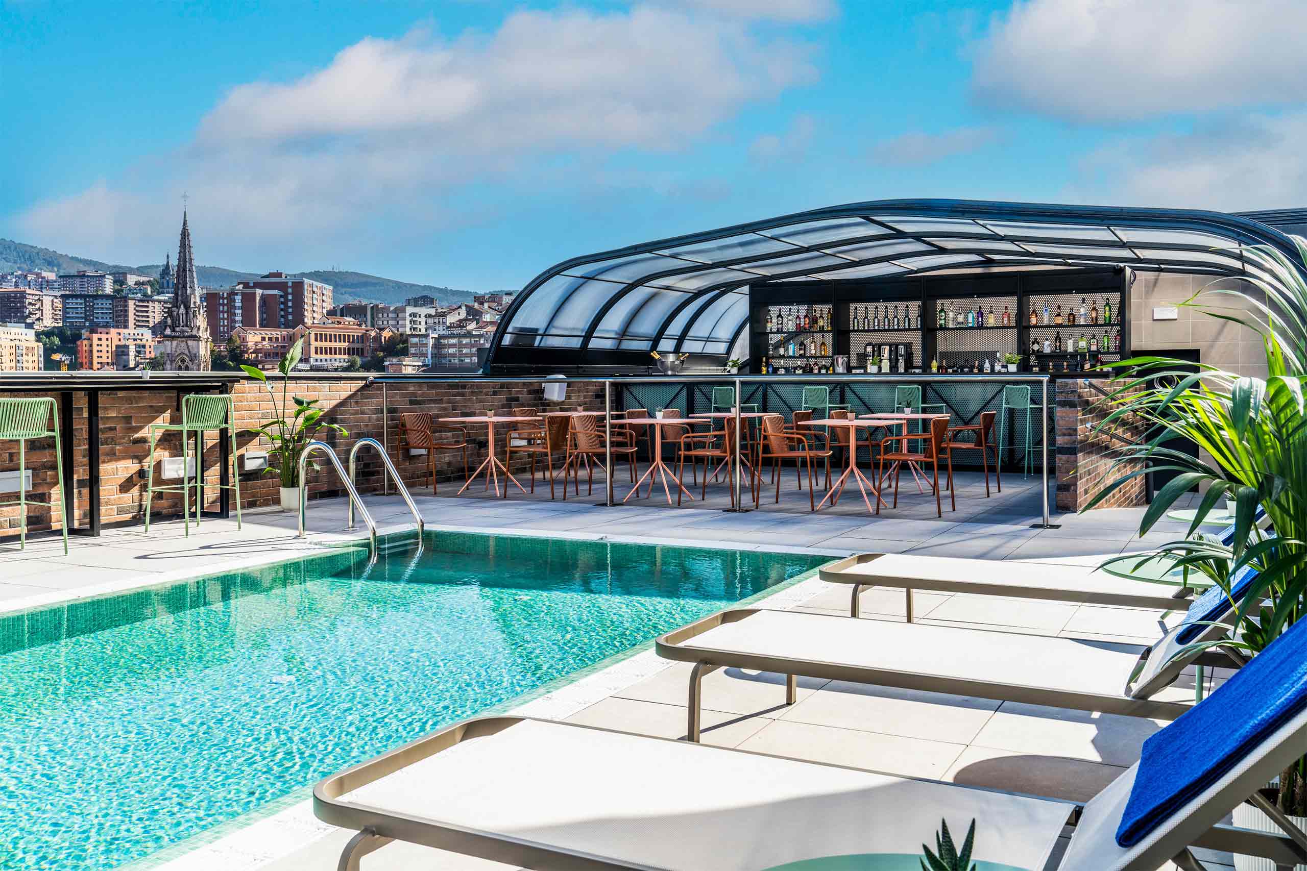 Rooftop Skybar at Axel Bilbao with a turquoise pool at the centre surrounded by sun loungers. Views of the city backdrop it.