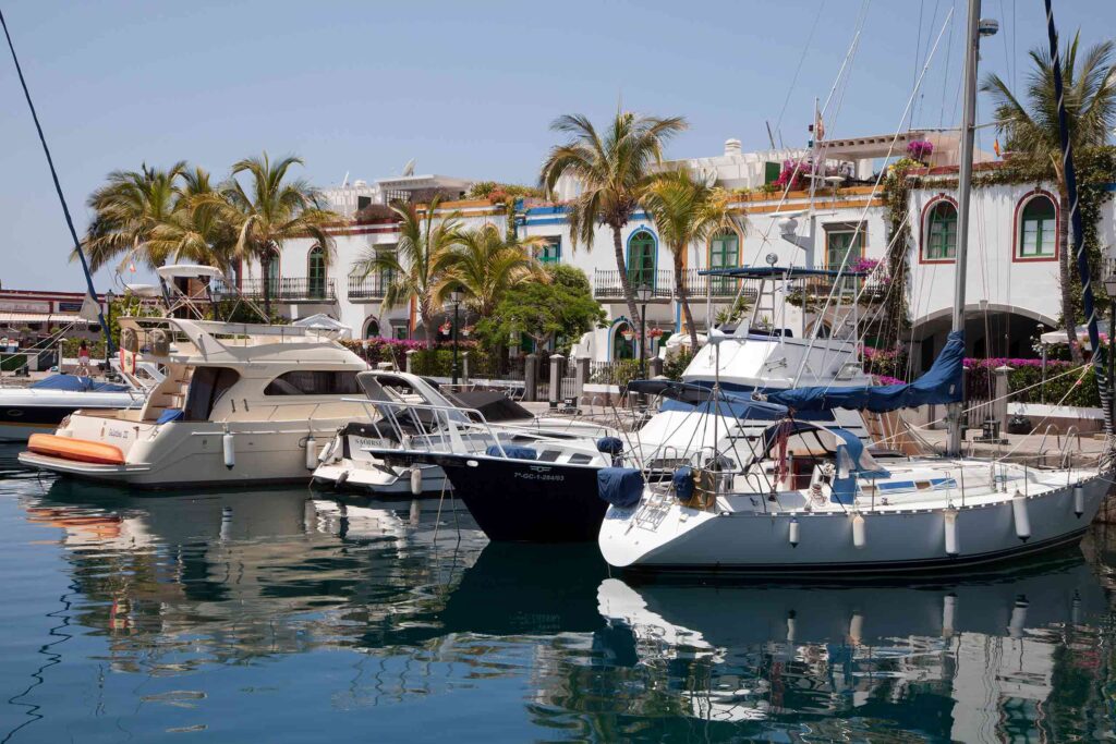 Small white pleasure yachts dock alongside old waterside houses in Mogan, Gran Canaria