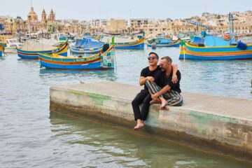 Two friends sitting on the pier at Marsaxlokk in Malta