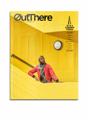 The It's a London Thing Issue of OutThere magazine, featuring a black model with a red jacket and brown and white scarf standing on a bright yellow stairwell